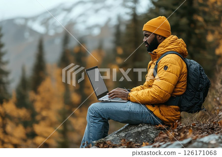 Man during hike sitting on a rock with a laptop on his lap. Remote work. Sitting on a rock, the man engages in remote work, showcasing the beauty of nature as his backdrop. 126171068