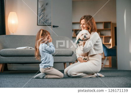 Woman is embracing the animal. Mother with daughter is at home with maltese dog 126171139