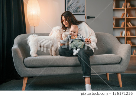 Woman with her toddler and cute white dog is indoors at home 126171236