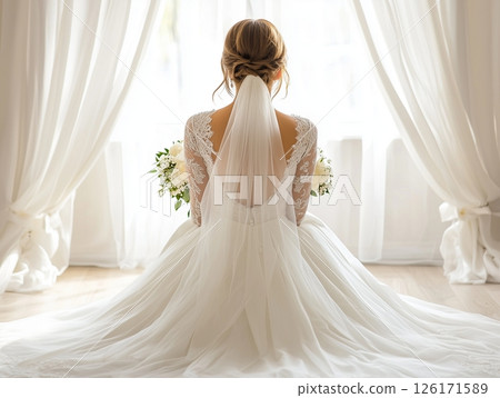 Bride sitting with back to camera in sunlit bright room, peaceful and soft wedding moment. 126171589