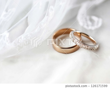 Wedding rings on white background with delicate lace fabric in soft focus behind. Wedding rings on white background with delicate lace fabric in soft focus behind. 126171599