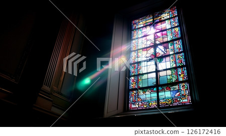 Stained glass window allows sunlight to create a colorful display inside an architectural space 126172416