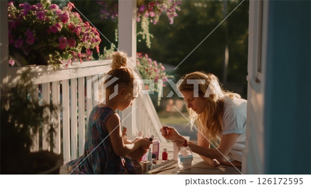 Mother and daughter enjoying a sunny afternoon while painting nails on the porch in a charming garden setting 126172595