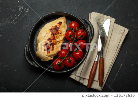 Grilled chicken breast fillet with cherry tomatoes in cast iron pan top view on rustic black background, healthy food 126172636