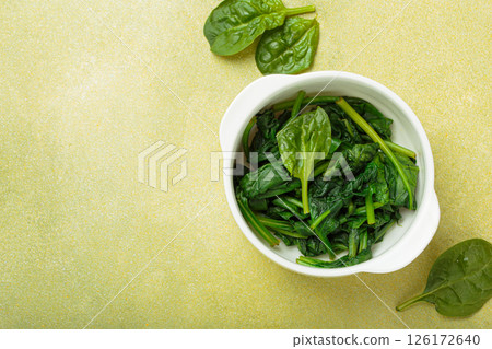 Steamed spinach leaves in white bowl on table top view on green background, healthy food or diet, space for text Steamed spinach leaves in white bowl on table top view on green background, healthy food or diet, space for text 126172640
