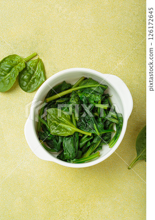Steamed spinach leaves in white bowl on table top view on green background, healthy food or diet 126172645