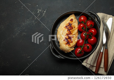 Grilled chicken breast fillet with cherry tomatoes in cast iron pan top view on rustic black background, healthy food, space for text 126172650