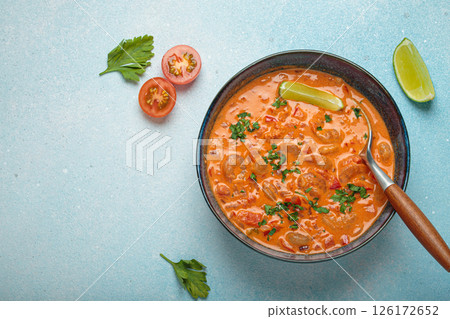 Brazilian traditional dish moqueca de camarao with shrimps, lime, peppers, and cilantro is served in a bowl on light blue background top view, space for text 126172652