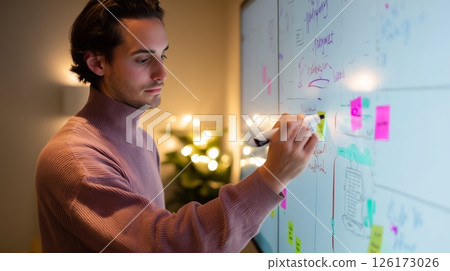 Creative brainstorming session in a cozy workspace with a young man writing on a digital board during evening hours 126173026