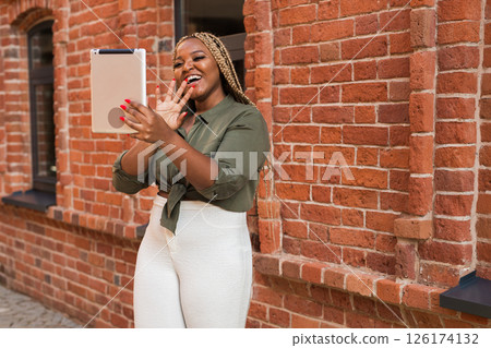 African american woman smiling and holding a tablet while walking on city. Communication, happiness, and digital connection with loved ones African american woman smiling and holding a tablet while walking on city. Communication, happiness, and digital connection with loved ones 126174132