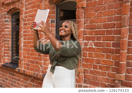 African american woman smiling and holding a tablet while walking on city. Communication, happiness, and digital connection with loved ones African american woman smiling and holding a tablet while walking on city. Communication, happiness, and digital connection with loved ones 126174133