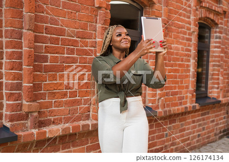 African american woman smiling and holding a tablet while walking on city. Communication, happiness, and digital connection with loved ones 126174134