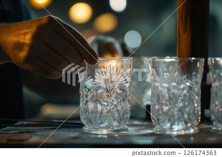 Glassblower inspecting a crystal glass for imperfections in a workshop lit by warm lights 126174363