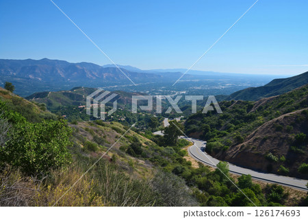 Winding road is making its way through lush green mountains to a sprawling city below 126174693