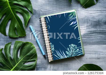 Notebook on a wood surface with tropical leaves and paper clips 126175384