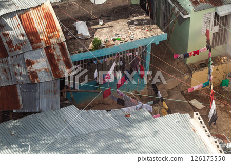 Washed laundry hangs to dry between rusty roofs at poor residential district Washed laundry hangs to dry between rusty roofs at poor residential district 126175550