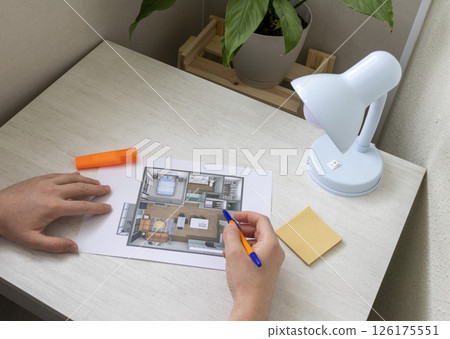 Man studies layout of the small, furnished apartment printed on the sheet of paper placed on the desk Man studies layout of the small, furnished apartment printed on the sheet of paper placed on the desk 126175551