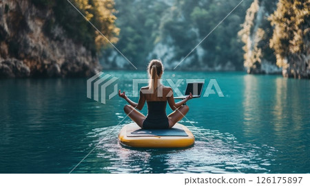 Woman meditating on paddleboard with laptop, serene lake. 126175897