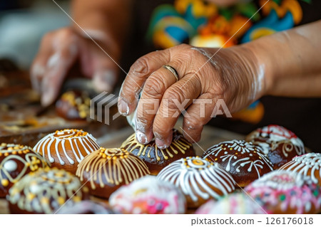 Baker carefully decorating a pan de muerto with white icing, a traditional sweet bread enjoyed during day of the dead celebrations in mexico 126176018