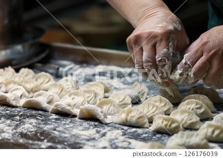 Close up of a cook's hands working with dough, shaping and preparing traditional asian dumplings on a wooden table 126176039