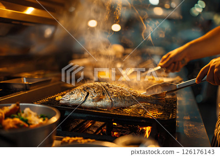 Whole fish is grilling over an open fire in a restaurant kitchen, smoke is rising from the grill Whole fish is grilling over an open fire in a restaurant kitchen, smoke is rising from the grill 126176143