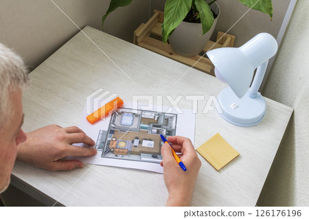 Man studies layout of the small, furnished apartment printed on the sheet of paper placed on the desk Man studies layout of the small, furnished apartment printed on the sheet of paper placed on the desk 126176196
