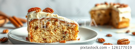 Delicious slice of homemade pecan cake served on a white plate with nuts and cinnamon in the background 126177019