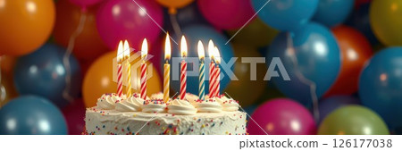 Celebratory birthday cake with lit candles surrounded by colorful balloons at a festive gathering 126177038