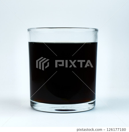 A clear glass contains a dark beverage against a white backdrop A clear glass contains a dark beverage against a white backdrop 126177180