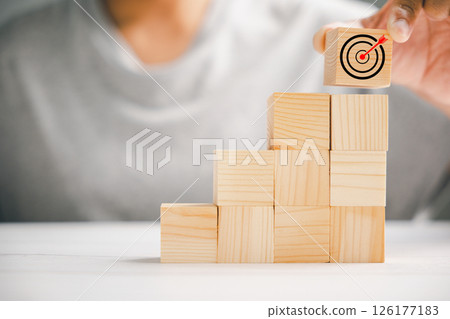 Hand arranging wood blocks to create a strategic stack, emphasizing the significance of a business strategy and action plan. Targeting business goals and success. 126177183