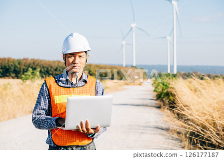 Engineer with laptop near wind turbines. A service technician ensures efficiency using innovation for landscape development. Working confidently ensuring quality in windmill service. 126177187
