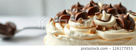 Delicious chocolate topped dessert garnished with swirls of cream and crunchy bits on a white table 126177853