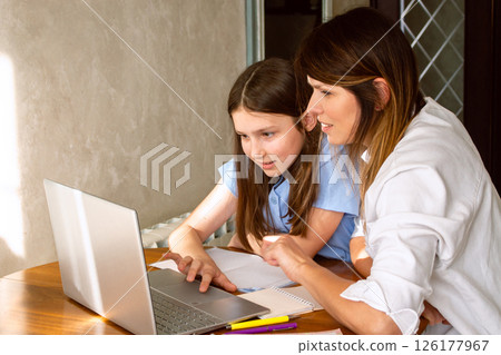 Happy mother with preteen daughter using laptop in home kitchen. Working on school project. Helping with homework using technologies. Happy mother with preteen daughter using laptop in home kitchen. Working on school project. Helping with homework using technologies. 126177967