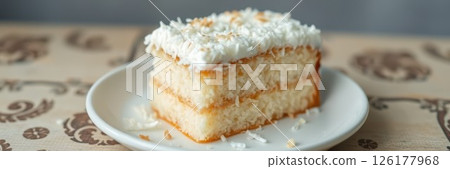Delicious coconut cake slice on a white plate resting on a decorative table with an inviting backdrop 126177968