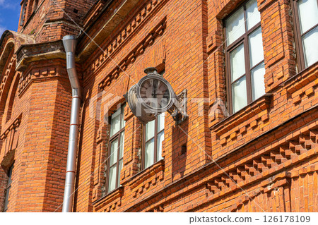 Old vintage street clock with greek numbers, old build with red bricks in the background. Old town. Old vintage street clock with greek numbers, old build with red bricks in the background. Old town. 126178109