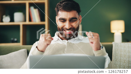 Man, fist pump and laptop on couch with celebration, excited and winning with online giveaway in home. Person, computer and happy with goal, success and profit with investment in living room at house 126178257