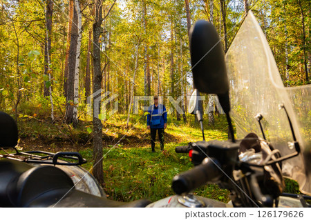 A person explores a lush green forest while parked Quad bike or ATV on a sunny day. Berry and mushroom picker A person explores a lush green forest while parked Quad bike or ATV on a sunny day. Berry and mushroom picker 126179626