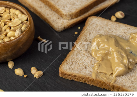 peanut butter on a piece of bread and roasted peanuts on the table, closeup 126180179