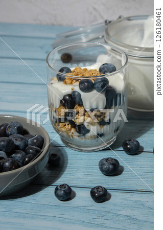 Preparing step by step Morning granola breakfast with homemade greek yogurt, blueberries in glasses on blue wooden background. Healthy diet Crunchy granola with yogurt nuts and blueberries 126180461