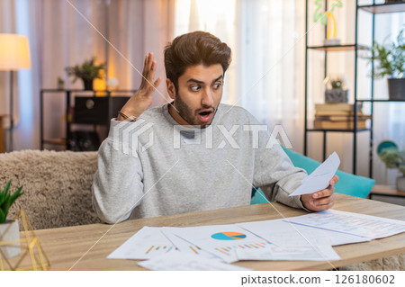 Young Indian man frustrated with bills and expenses while reviewing documents at home on table 126180602