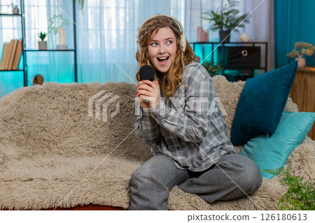 Woman on sofa singing with microphone wearing headphones moving joyfully to music feeling like star Woman on sofa singing with microphone wearing headphones moving joyfully to music feeling like star 126180613