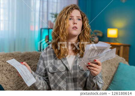 Woman sits on sofa holding bills and receipts worried with head in hands stressed by money problems 126180614