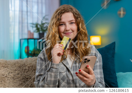 Young woman sitting on sofa holding bank card and smartphone making online payment or money transfer Young woman sitting on sofa holding bank card and smartphone making online payment or money transfer 126180615