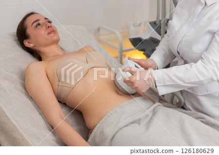 Woman receiving LPG vacuum massage on belly area by cosmetologist using modern equipment in clinic Woman receiving LPG vacuum massage on belly area by cosmetologist using modern equipment in clinic 126180629
