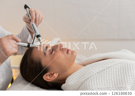 Beautician doctor makes woman micro currents face therapy using electrical impulses in spa salon 126180630