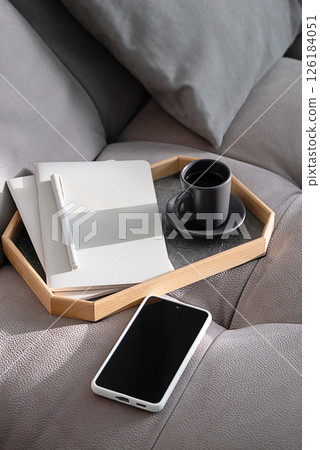 Cozy Morning Setup with Coffee Cup, Notebook and Smartphone on Comfortable Grey Sofa. Relaxation and Planning Concept. 126184051