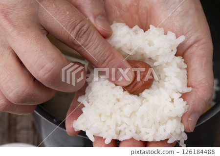 The process of putting pickled plums into the rice balls and making them 126184488