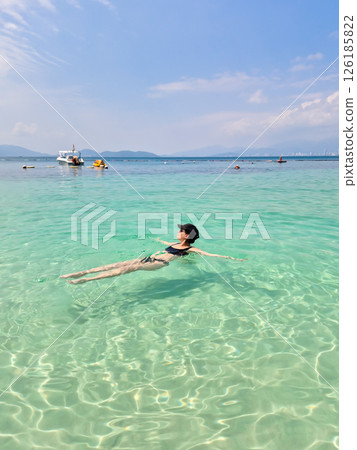 A brunette Russian girl in a black swimsuit and cap relaxes on Nha Trang beach. Sunny day, South China Sea, Vietnam. A brunette Russian girl in a black swimsuit and cap relaxes on Nha Trang beach. Sunny day, South China Sea, Vietnam. 126185822