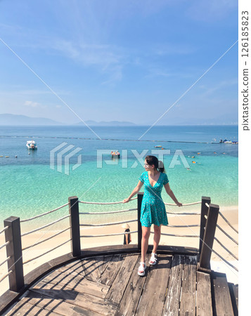 Russian tourist in blue dress enjoying Vietnam beach vacation. Aerial view from pier showing crystal clear water and white sand in Nha Trang. 126185823