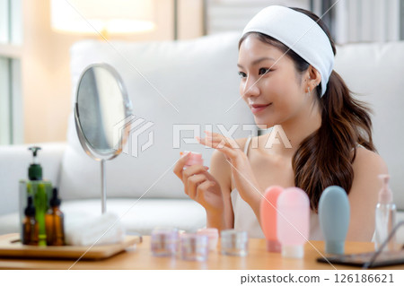 Beauty young asian woman applying cream or lotion while looking mirror in living room. 126186621